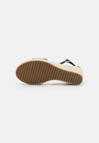 Sandaler med en teksturert såle av naturlig fiber, svarte stropper og en liten metalldetalj. Sålen har horisontale riller for grep.