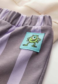 Tessuto a righe grigio e lavanda con elastico in vita, caratterizzato da una toppa blu con un personaggio cartoon di un mostro verde.