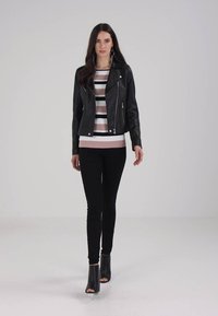 Svart skinnsykkeljakke med sølvglidelåser, brukt over en stripete rosa og hvit genser, sammen med svarte skinny jeans og høyhælte støvletter.