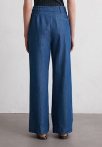 Wide-leg denim trousers in a deep blue, made of soft fabric. Features a back pocket and a clean hem with a subtle texture.