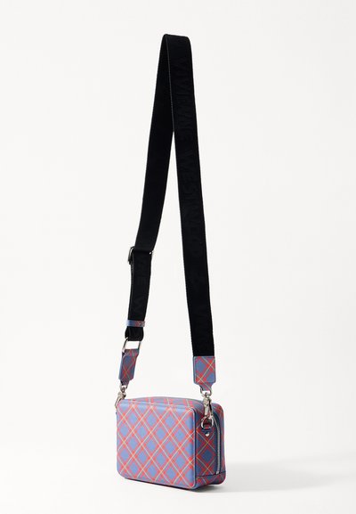Sac bandoulière rectangulaire bleu avec un motif tartan rouge. Dispose d'une bandoulière en tissu noir avec lettrage, de quincaillerie en argent et d'une fermeture éclair.