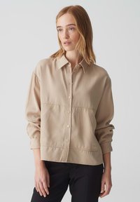 Beige overhemd met knopen, een kraag, lange mouwen en een relaxte pasvorm. Bevat zichtbare stiksels en twee voorkezen. Glad stoftextuur.