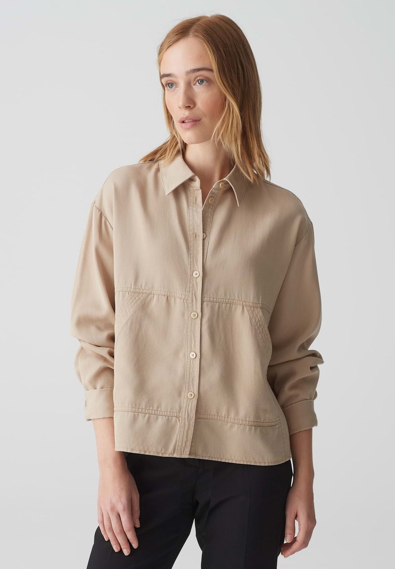 Beige overhemd met knopen, een kraag, lange mouwen en een relaxte pasvorm. Bevat zichtbare stiksels en twee voorkezen. Glad stoftextuur.
