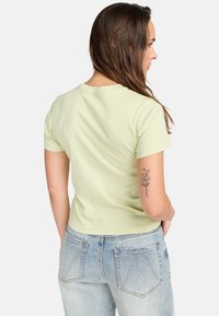 Light green, short-sleeve t-shirt with a round neckline. Soft fabric and fitted design. Worn with high-waisted light blue jeans.