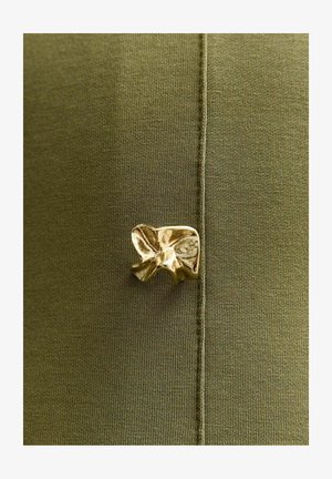 Tela verde oliva con una textura suave que presenta un detalle de lazo metálico dorado adherido en la costura. Se aprecian detalles de costura.