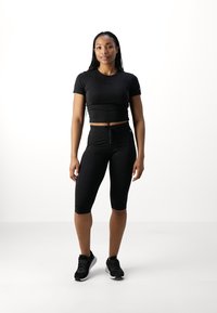 Conjunto deportivo negro que incluye una camiseta ajustada de manga corta y leggings hasta la rodilla con cintura de cordón. Tela texturada, diseño elegante.