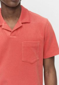 Korte mouwen, koraalkleurige polo met een zachte katoen. Voorzien van een klassieke kraag en een borstzak. Gladde textuur, minimalistisch ontwerp.