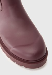 Botte en caoutchouc violet avec un bout arrondi, texture lisse et semelle épaisse comportant un léger motif de crampons à la base.