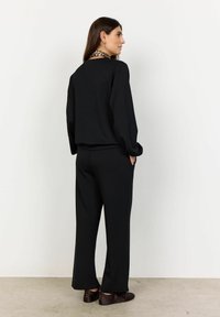 Must värv loungewear komplekt, mis on lõdva lõikega. Ülal on pikad varrukad ja ümar kaelus; pükstel on laiad sääred ja küljetaskud.