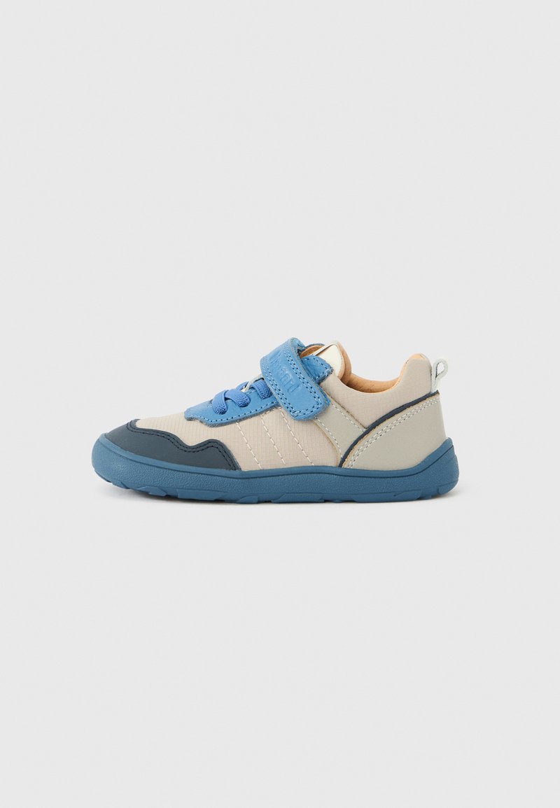 Beige en blauwe kindersneaker met blauwe elastische veters, een blauwe klittenbandsluiting en een donkerblauwe zool op een effen lichte achtergrond.