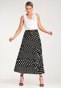 Czarna i biała spódnica w grochy z warstwowymi panelami i brązowym paskiem, zestawiona z białą satynową bluzką i czarnymi sandałkami na szpilkach.