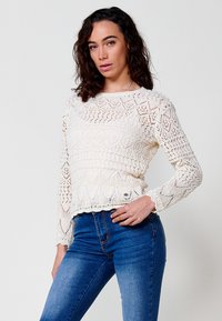 Suéter de punto color crema con patrones geométricos, mangas largas y dobladillo acanalado, combinado con jeans de tiro alto azules.
