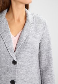 Blazer de mezcla de lana gris con solapa, mangas largas y dos botones negros. Tejido texturizado con un acabado suave. Capa interior en forma de V visible.
