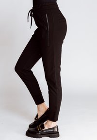 Schwarze Jogginghosen mit Muster und schmaler Passform, mit Kordelzug in der Taille und seitlichen Reißverschlusstaschen, kombiniert mit schwarzen, klobigen Loafers.