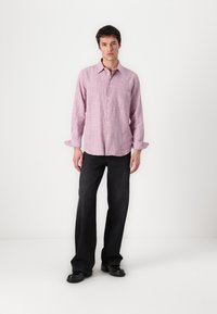 Checked pink long-sleeve shirt with a pocket, paired with black loose-fitting trousers and black shoes. Clean, minimalistic design.