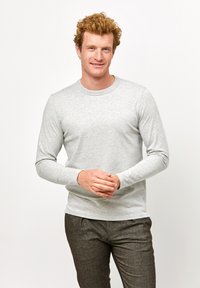 Hellgraues Langarmshirt aus einem weichen, strukturierten Stoff; runder Ausschnitt; taillierte Passform; getragen mit dunklen, maßgeschneiderten Hosen.