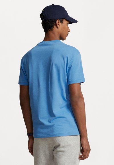 Tricou albastru cu mânecă scurtă, din bumbac, cu guler rotund și un design simplu. Purtați-l cu pantaloni gri deschis și o șapcă albastră.