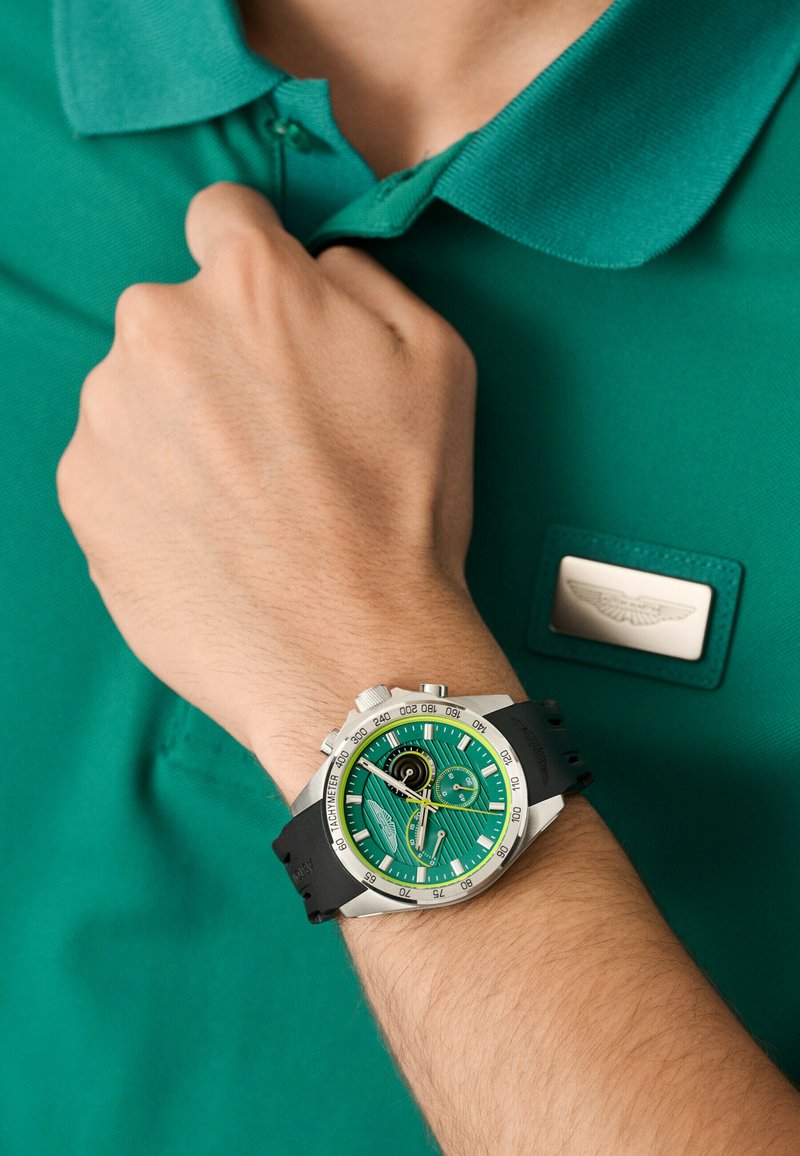 Orologio verde con quadrante testurizzato e dettagli in acciaio inox, cinturino in gomma e cassa in acciaio inox, abbinato a una polo verde.