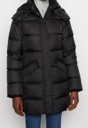 Henkilö, jolla on musta toppatakki, jossa on etutaskut ja vetoketju, yhdistettynä sinisiin farkkuihin ja vaaleanharmaaseen neulepuseroon.