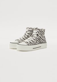 Svarte og hvite zebra-stripete høye sneakers med hvite lisser, med en tykk hvit gummisåle og svarte horisontale stripe detaljer.