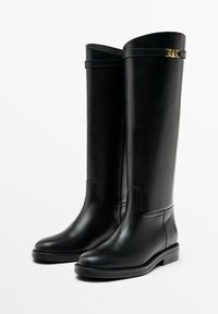 Černé kožené kozačky až ke kolenům s hladkým povrchem, kulatou špičkou, nízkým blokovým podpatkem a ozdobnými zlatými kovovými doplňky na horní straně.