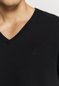 Zwarte geribde V-hals sweater met subtiele s.Oliver branding op de borst. De zachte textuur en snug fit verhogen het comfort.