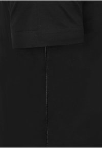 Czarna koszulka z krótkim rękawem o prostym kroju, z widocznym przeszyciem wzdłuż bocznego szwu. Materiał ma gładką fakturę.