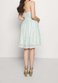 Mintgrön spetsklänning med en åtsittande överdel och utsvängd kjol. Har spaghettistöd och en vågig nederkant. Matchas med olivgröna klumpiga klackar.