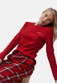 Camisa roja de manga larga con textura acanalada que presenta bordado de "Ho Ho Ho", acompañada de pantalones de pijama a cuadros rojos con acentos en blanco y verde.