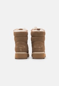 Bottines en daim marron avec doublure en fausse fourrure beige, dotées d'un design simple et d'un patch logo Roxy à l'arrière. Semelles en caoutchouc plates.