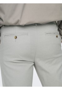 Pantalones gris claro con una tela texturizada, que cuentan con dos bolsillos traseros, cada uno con una abertura horizontal y un acento de botón redondo.