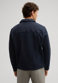 Giacca di jeans blu navy con colletto, dettagli in bottoni e tasche laterali, caratterizzata da una texture liscia e un taglio su misura. Vista posteriore mostrata.