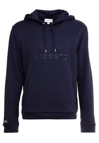 Námornícky modrá mikina s kapucí, vyšívané logo "LACOSTE", klokaní kapsa, texturovaná látka a zelené logo krokodýla na rukávu.