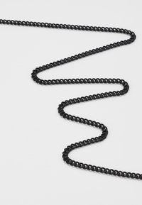 Svart metallkjede med sammenkoblede ovale ledd, som viser en jevn overflate og en fleksibel, zigzag-form mot en hvit bakgrunn.