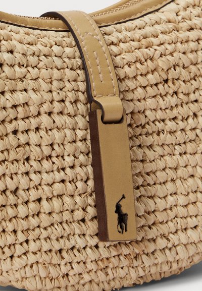 Υφαντή τσάντα από άχυρο σε φυσικό μπεζ χρώμα με λείο δερμάτινο ιμάντα σε ταμπά απόχρωση που διαθέτει ανάγλυφο σκοτεινό λογότυπο. Κλείσιμο με φερμουάρ στην κορυφή.