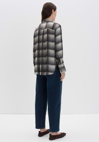 Camicia a scacchi bianca e nera con maniche lunghe e colletto, abbinata a jeans scuri larghi e ballerine marroni, mostrata da dietro.