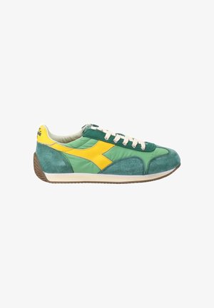 Baskets de sport vertes et jaunes avec des lacets blancs, des panneaux en daim et tissu, et une semelle marron rainurée, vues du côté intérieur.