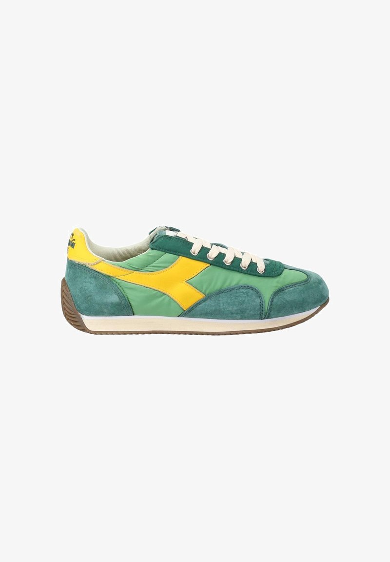 Baskets de sport vertes et jaunes avec des lacets blancs, des panneaux en daim et tissu, et une semelle marron rainurée, vues du côté intérieur.