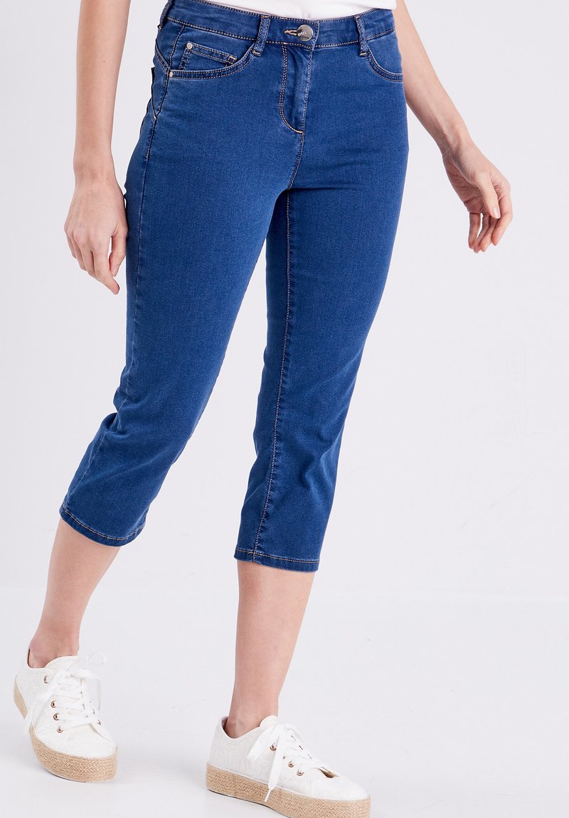 Donkerblauwe denim capri broeken met een slim fit ontwerp, vijf zakken en contrasterende stiksels. Gecombineerd met witte plateau sneakers.