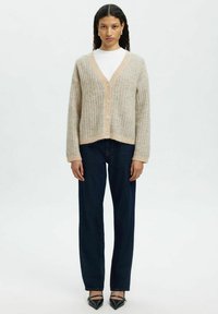 Beige ribbattu cardigan, johon kuuluu V-kaula-auko, viisi nappia ja lyhyt malli. Yhdistetty tummansinisien suoranlahkeisten farkkujen ja mustien teräväkärkisten kenkien kanssa.
