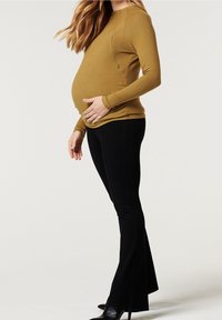 Těhotenský top v hořčicové barvě s dlouhými rukávy a bočním zipem, doplněný o černé zvonové kalhoty a boty na podpatku.