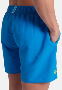 Pantaloni da bagno blu con cintura elastica, tasche laterali e logo sull'orlo inferiore. Tessuto liscio con una consistenza leggera.