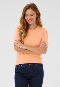 Pull-over à manches courtes en doux tricot orange. Doté d'un col rond, coupe décontractée, et assorti à un jean bleu foncé. Texturé lisse.