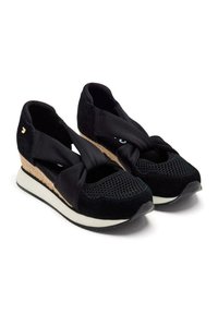 Zapatillas deportivas negras con parte superior de malla y ante, correas de tela trenzada y tacón de corcho en cuña. Suela exterior de goma blanca para tracción.