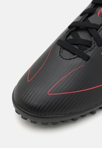 Schwarze Fußballschuhe mit geripptem Muster, ausgestattet mit roten Akzenten und schwarzen Schnürsenkeln. Enthält eine abgerundete Spitze und geformte Noppen für besseren Halt.