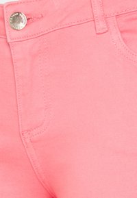 Primer plano de unos vaqueros de mezclilla rosa que muestran detalles del botón, el lazo del cinturón, las costuras y los bolsillos.
