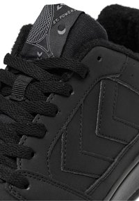 Czarny sneaker z fakturowaną cholewką, zdobiony wzorem w zygzak, płaskie sznurowadła oraz wyściełany język z logo, na tle materiału.