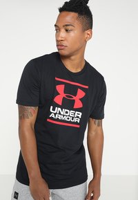 Camiseta negra de manga corta hecha de algodón, con un logo rojo de Under Armour en el pecho, que presenta una textura suave y un corte clásico.