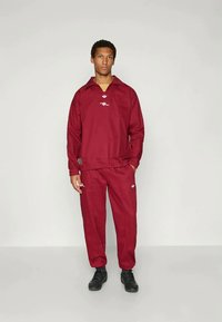 Maroon track jacket with a collar, featuring a white logo; paired with matching pants. Both garments are made of smooth fabric.