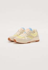 Baskets beiges et jaunes avec une accent bleue et rose. Comprend des matériaux en daim et en maille, une semelle rembourrée et des lacets épais.